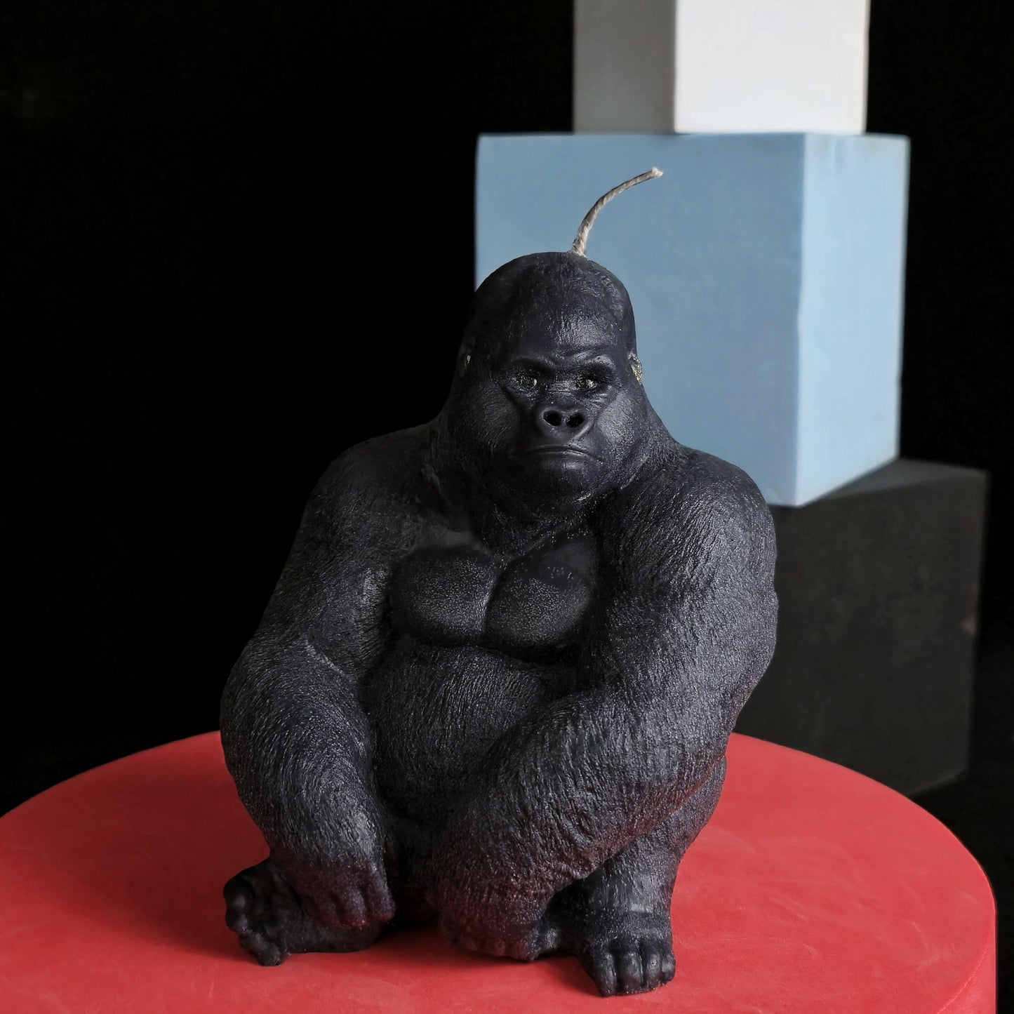 Sculpted black gorilla soy wax candle in seated pose, muscular and detailed, displayed on red pedestal with dark background