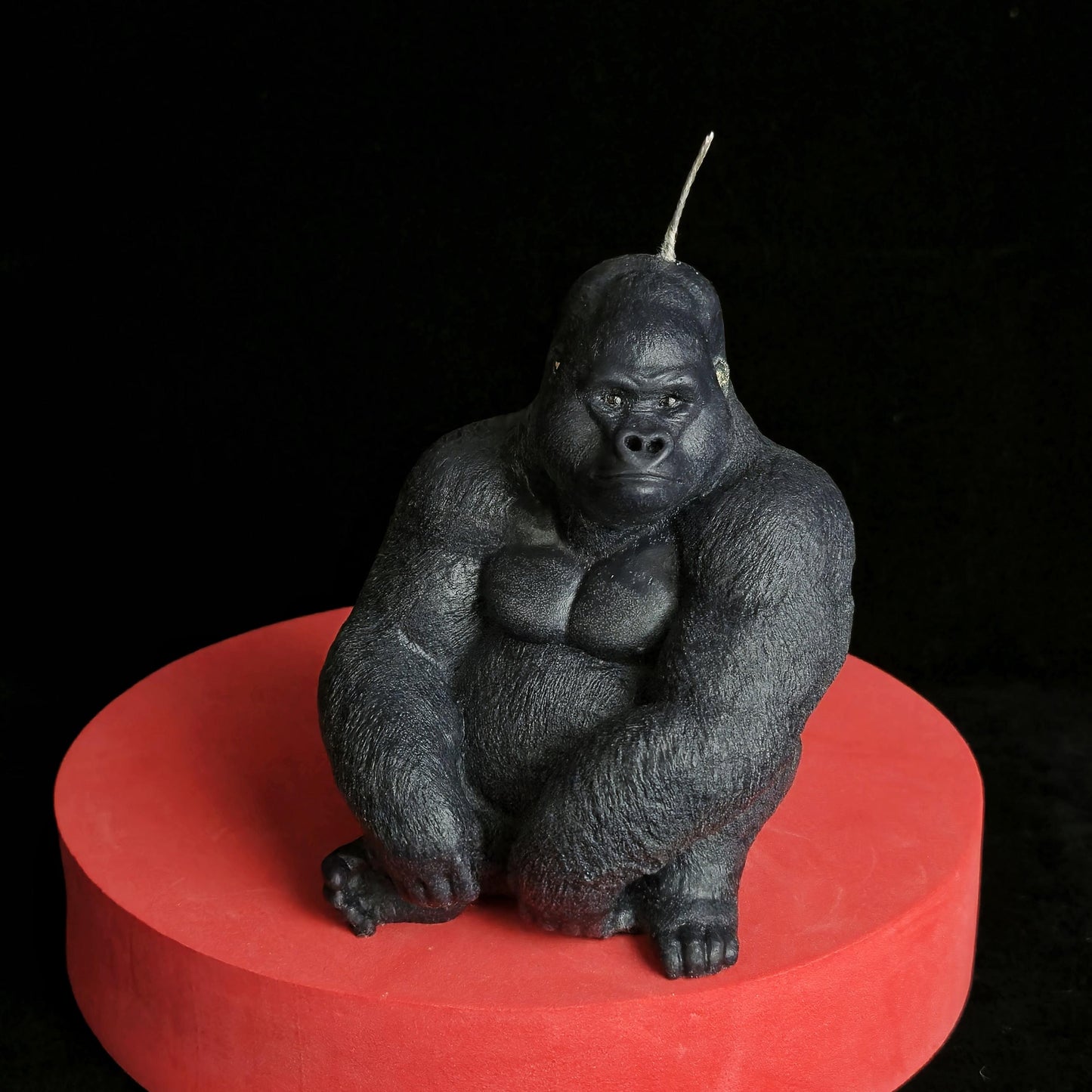 Sculpted black gorilla soy wax candle in seated pose, muscular and detailed, displayed on red pedestal with dark background