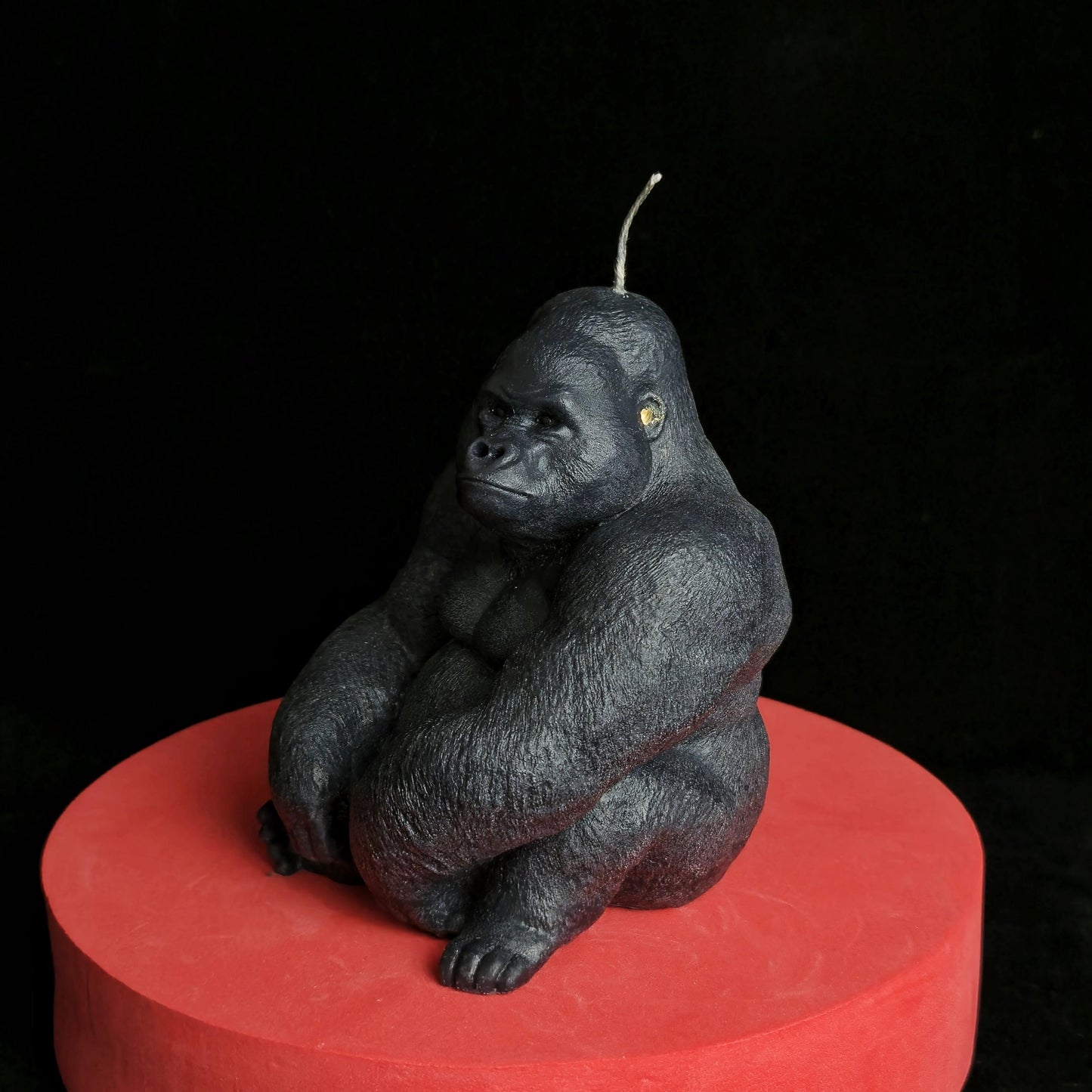 Sculpted black gorilla soy wax candle in seated pose, muscular and detailed, displayed on red pedestal with dark background