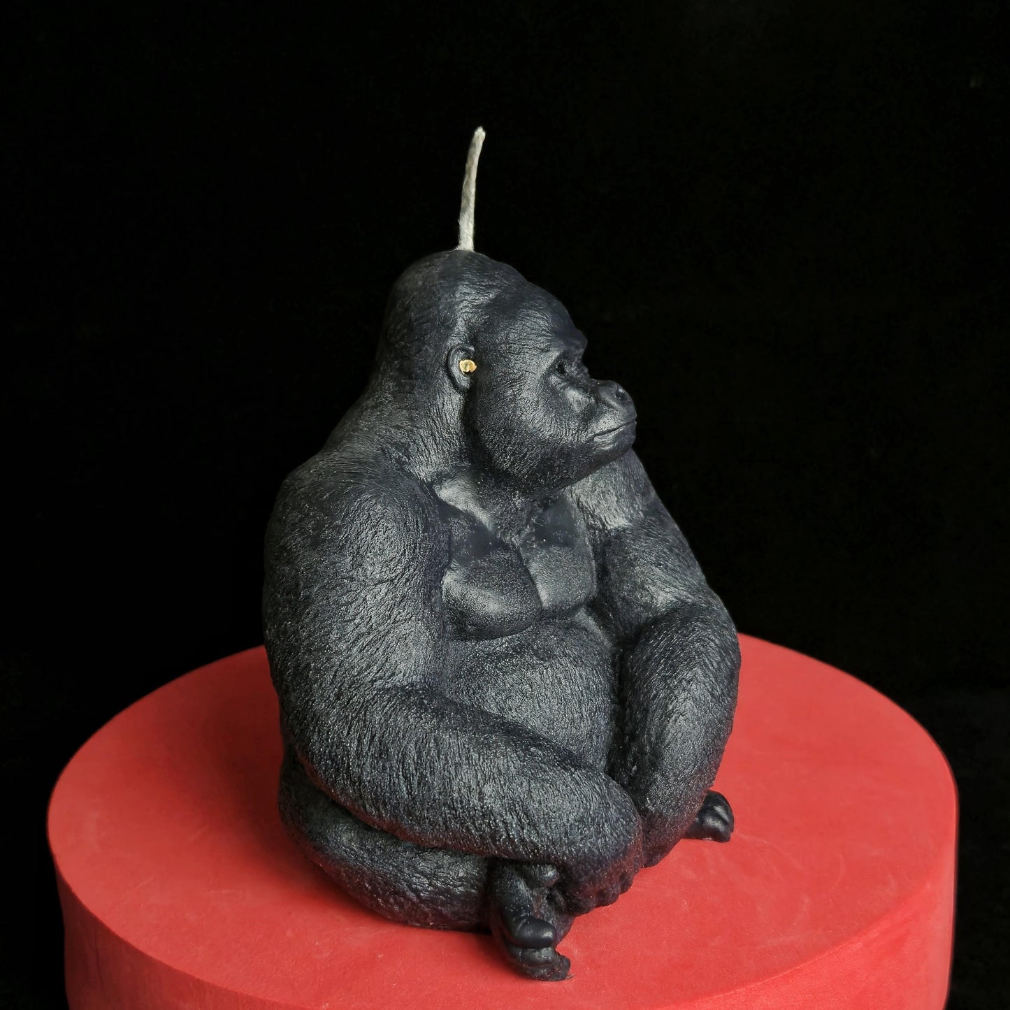 Sculpted black gorilla soy wax candle in seated pose, muscular and detailed, displayed on red pedestal with dark background