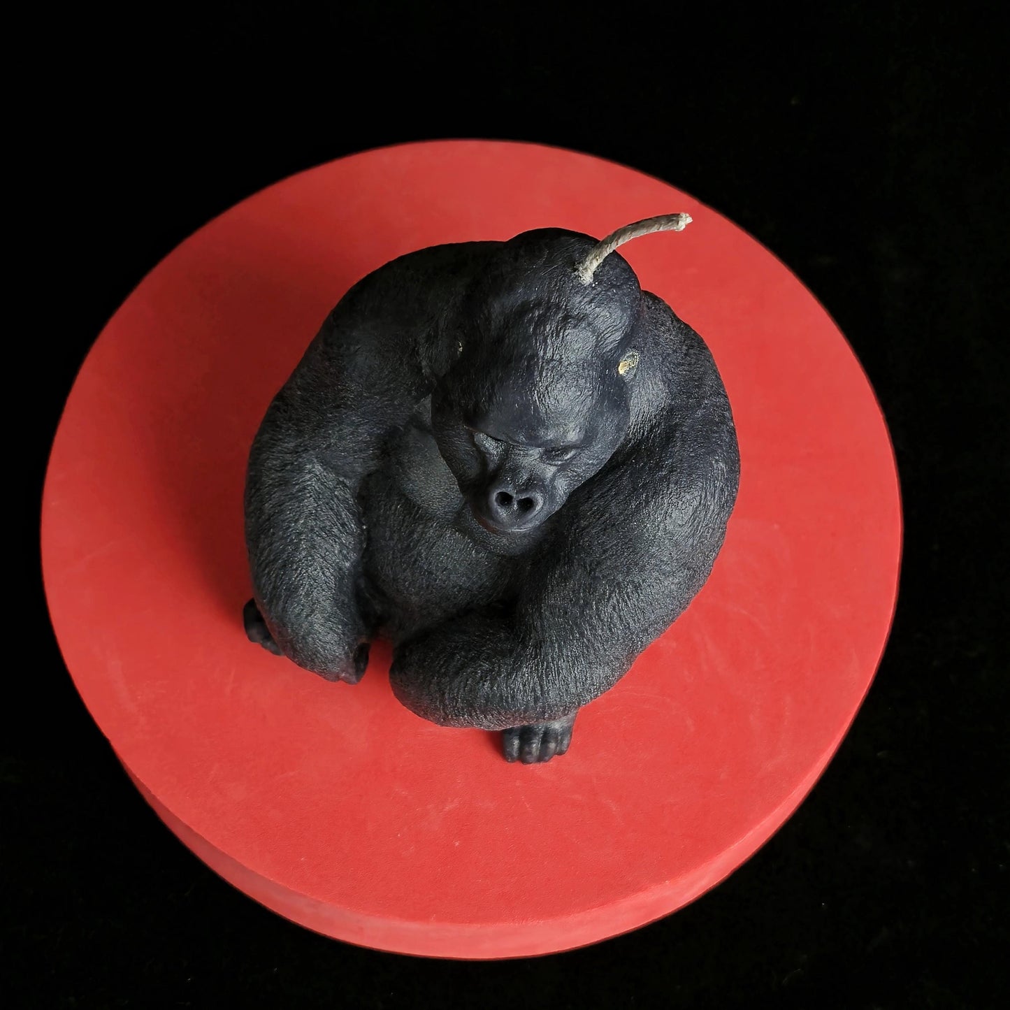 Sculpted black gorilla soy wax candle in seated pose, muscular and detailed, displayed on red pedestal with dark background
