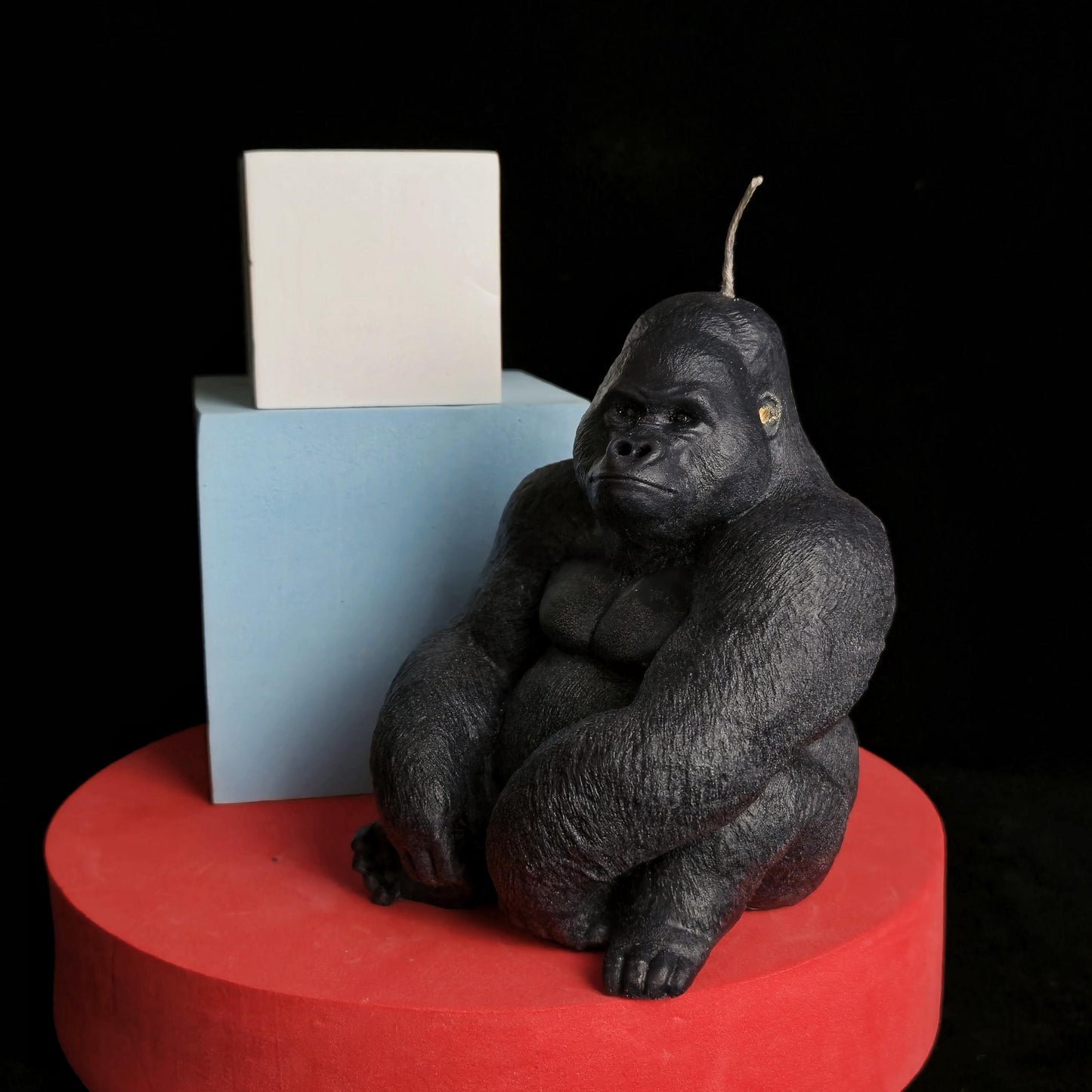 Sculpted black gorilla soy wax candle in seated pose, muscular and detailed, displayed on red pedestal with dark background