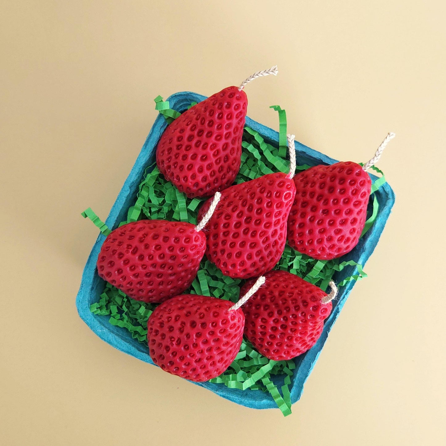 A realistic basket of strawberry candles, strawberry set candle, blue pulp basket of strawberries, red strawberry with wick on yellow background, green crinkle cut paper inside, gift of cake topper, birthday strawberry topper, berry with holes, looks like real strawberry, birthday candles, home decor, kitchen decor candles, giving off a sweet strawberry scent, juicy strawberry, strawberry-shaped soy candles