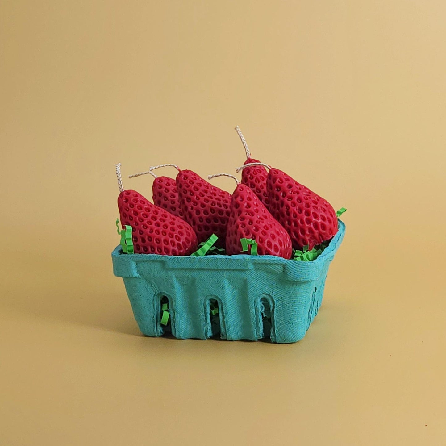 A realistic basket of strawberry candles, strawberry set candle, blue pulp basket of strawberries, red strawberry with wick on yellow background, green crinkle cut paper inside, gift of cake topper, birthday strawberry topper, berry with holes, looks like real strawberry, birthday candles, home decor, kitchen decor candles, giving off a sweet strawberry scent, juicy strawberry, strawberry-shaped soy candles
