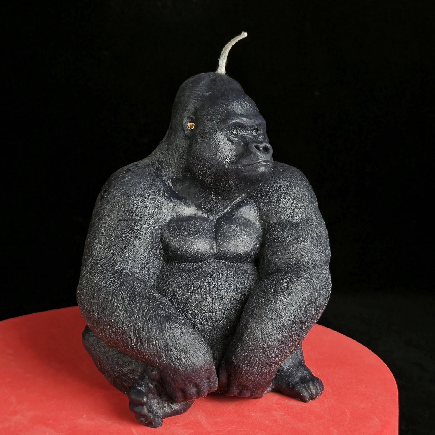 Sculpted black gorilla soy wax candle in seated pose, muscular and detailed, displayed on red pedestal with dark background