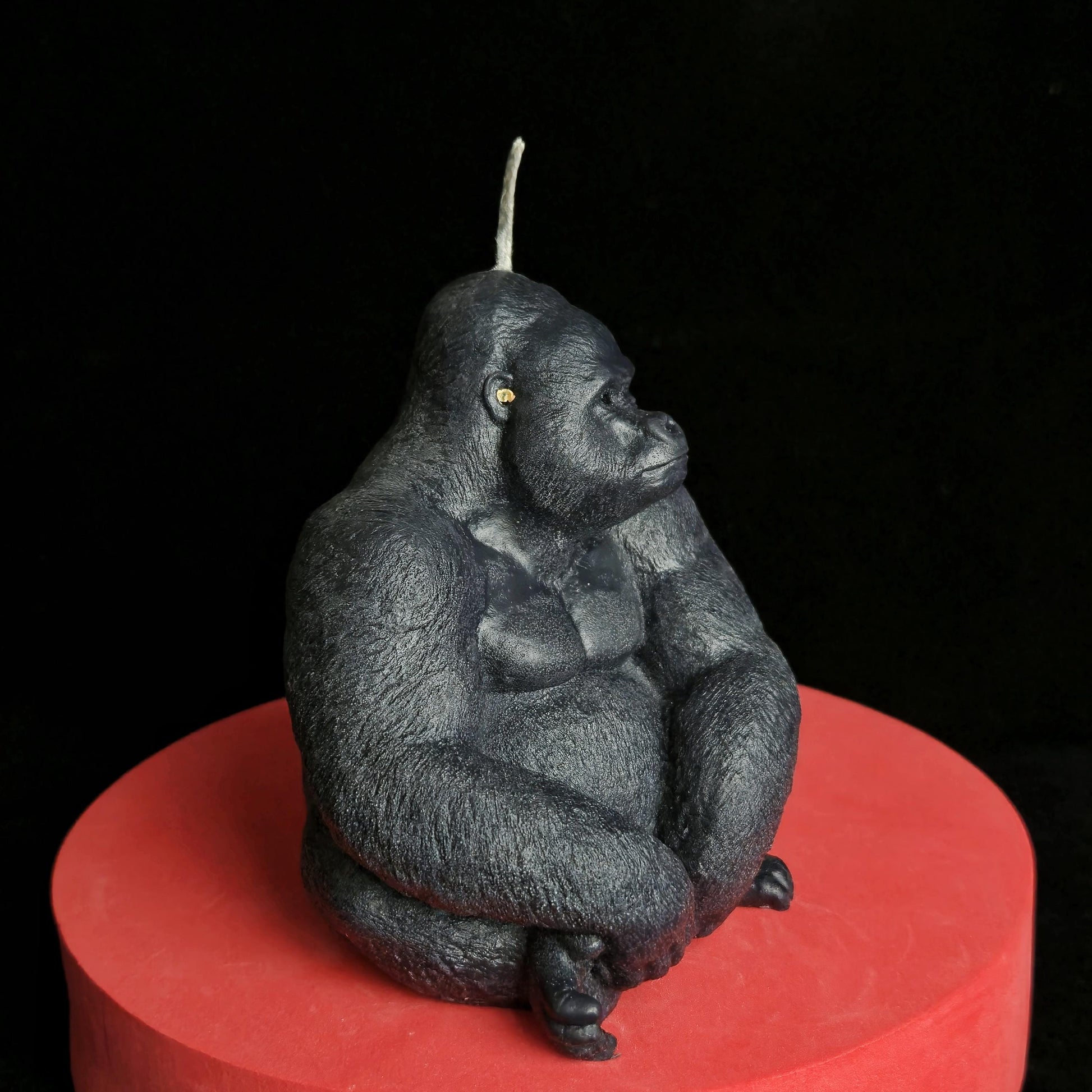 Sculpted black gorilla soy wax candle in seated pose, muscular and detailed, displayed on red pedestal with dark background