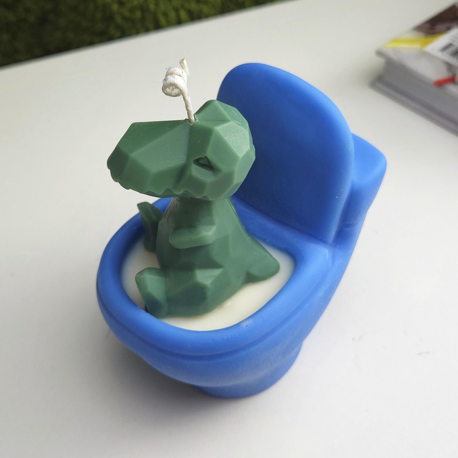 Handmade soy wax candle shaped like a green dinosaur sitting on a blue toilet, funny novelty gag gift
