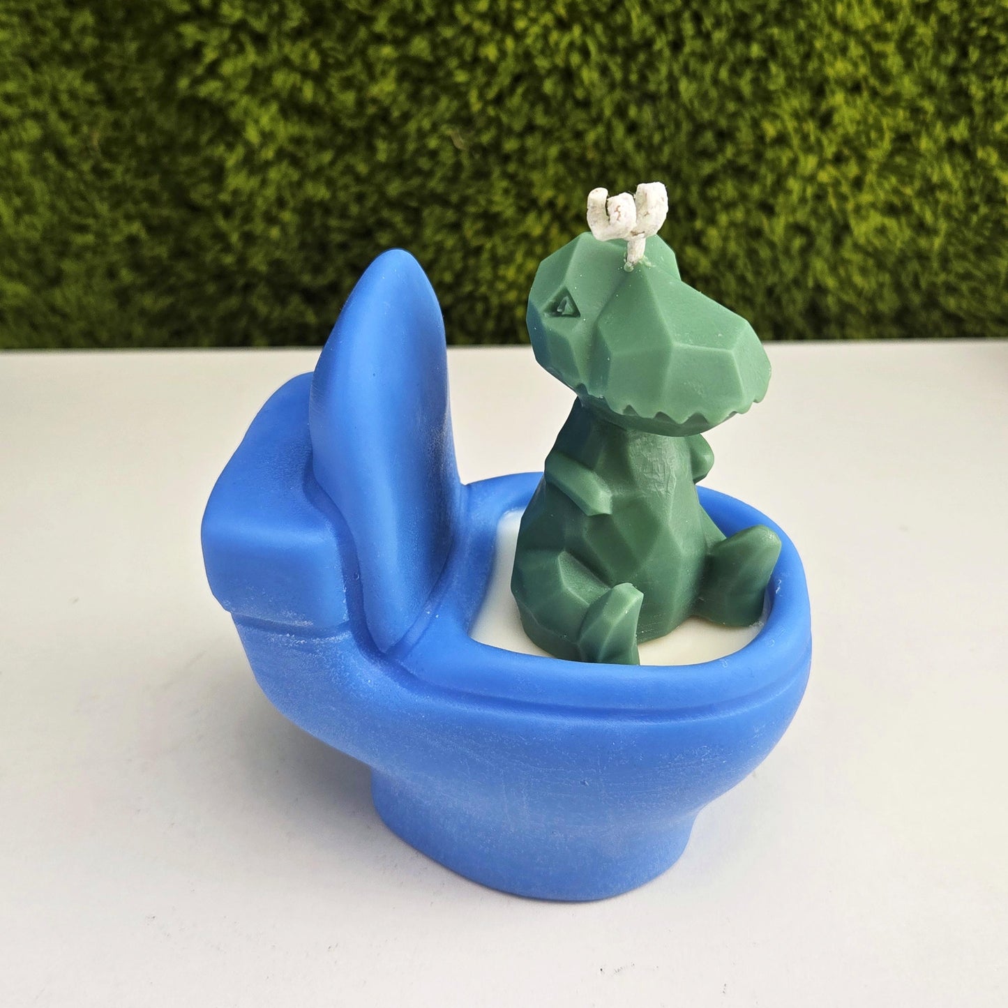 Handmade soy wax candle shaped like a green dinosaur sitting on a blue toilet, funny novelty gag gift