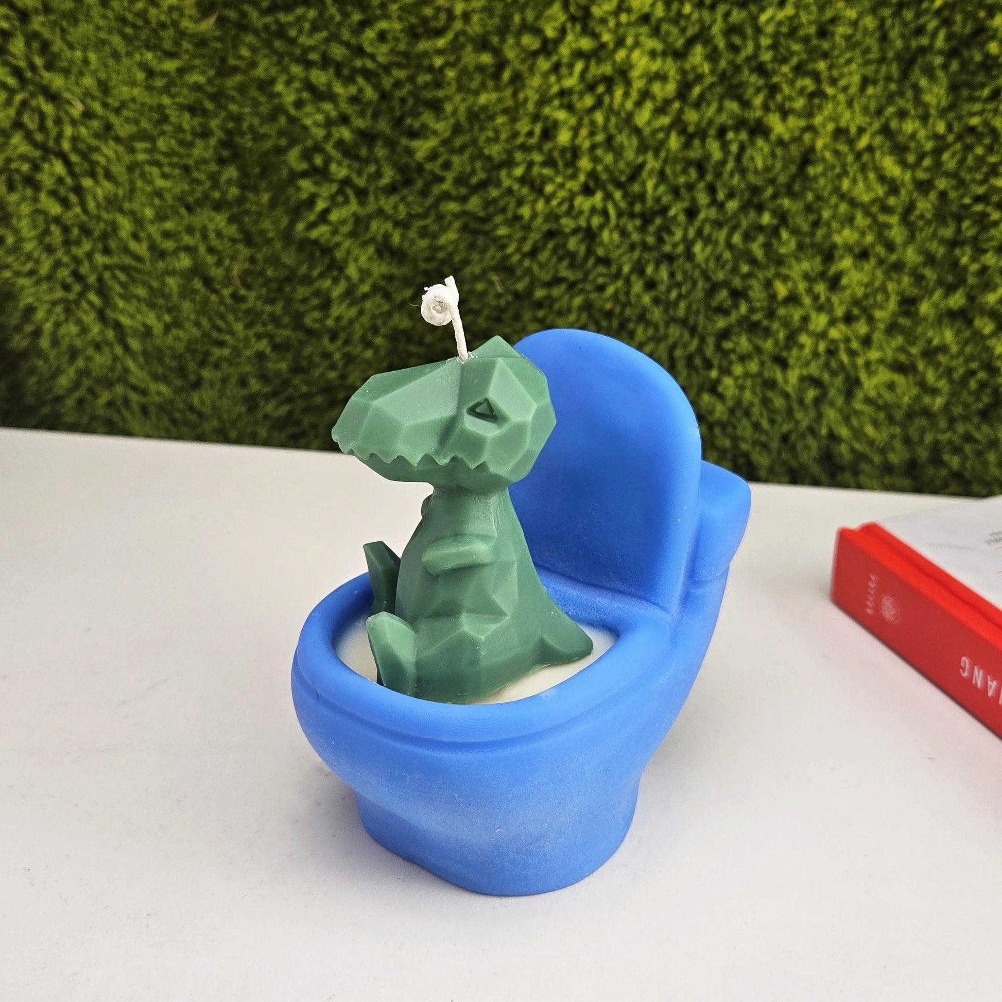 Handmade soy wax candle shaped like a green dinosaur sitting on a blue toilet, funny novelty gag gift