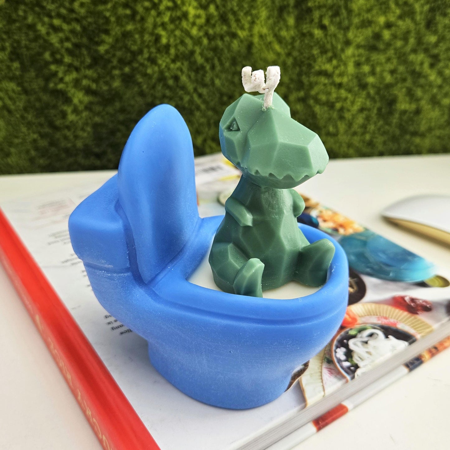 Handmade soy wax candle shaped like a green dinosaur sitting on a blue toilet, funny novelty gag gift